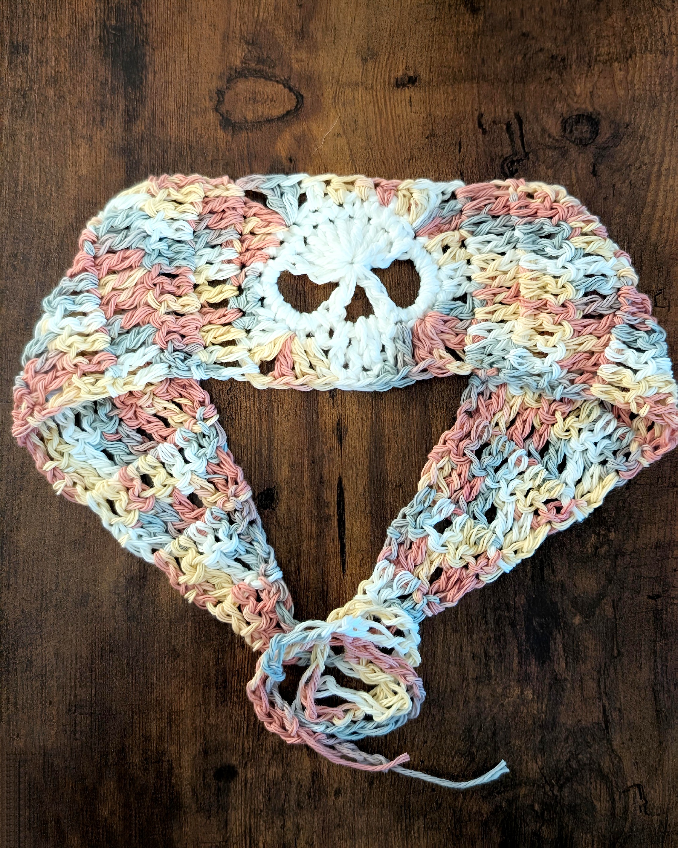 Handmade crochet headband featuring a skull design in pastel colors, displayed on a wooden surface.